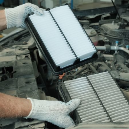 Car maintenance in a car service center. An auto mechanic holds a used air filter and a new engine air filter in his hands, demonstrating the degree of contamination.